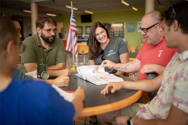 group of adults gathered around a table in a bright room with an American flag