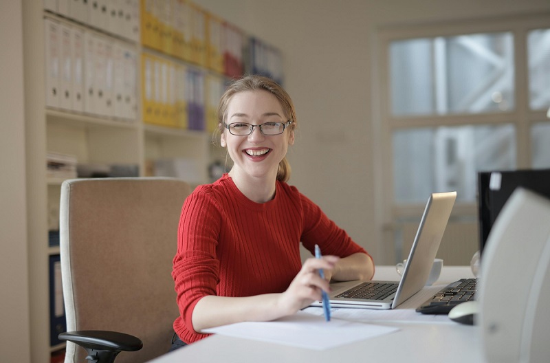 a woman in a red sweater and glasses sits at a white desk