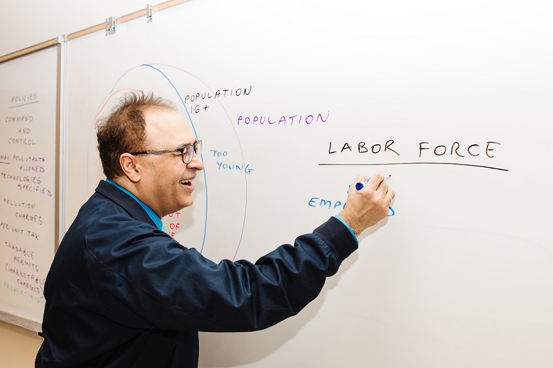 a middle aged man in glasses smiling while writing on a whiteboard