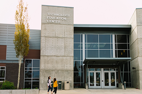 An outside shot of the Redmond Technology Education Center building, with two students walking toward the door in the foreground