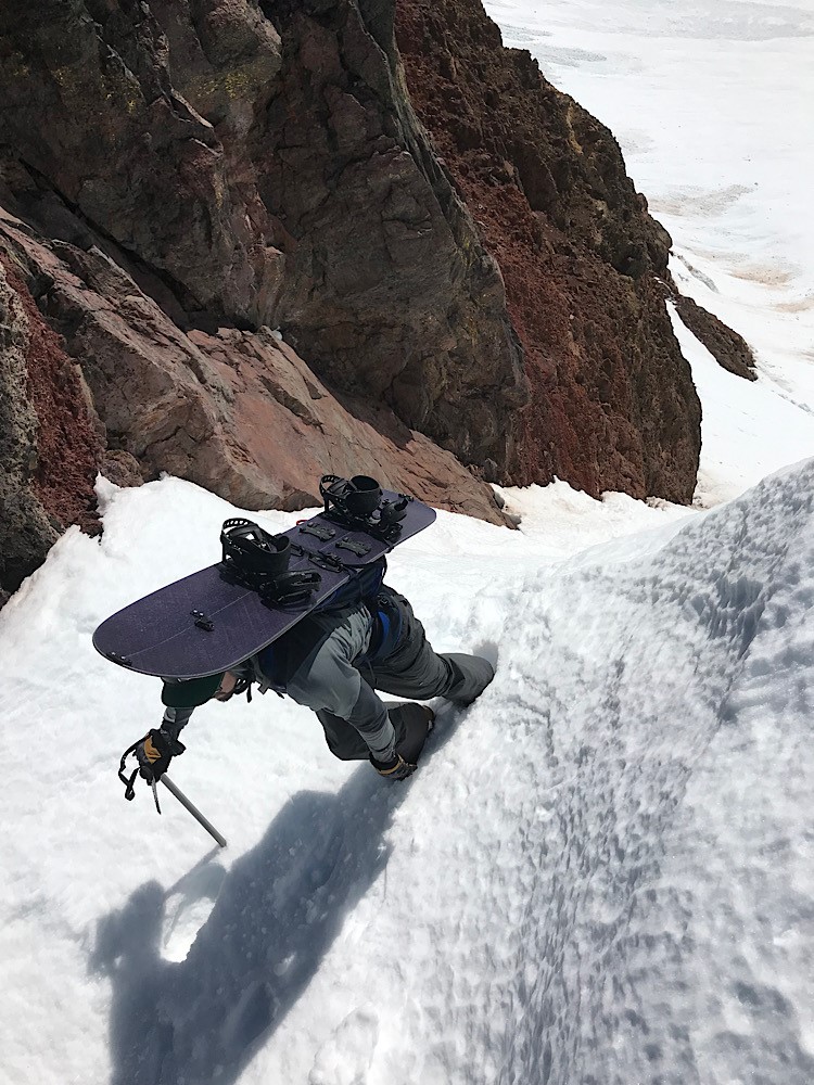 Snowboarder ckimbing a tight chute with ice axe