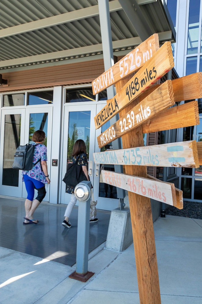 Two students walking into a building next to a mileage signpost indicating Central and South American countries. 