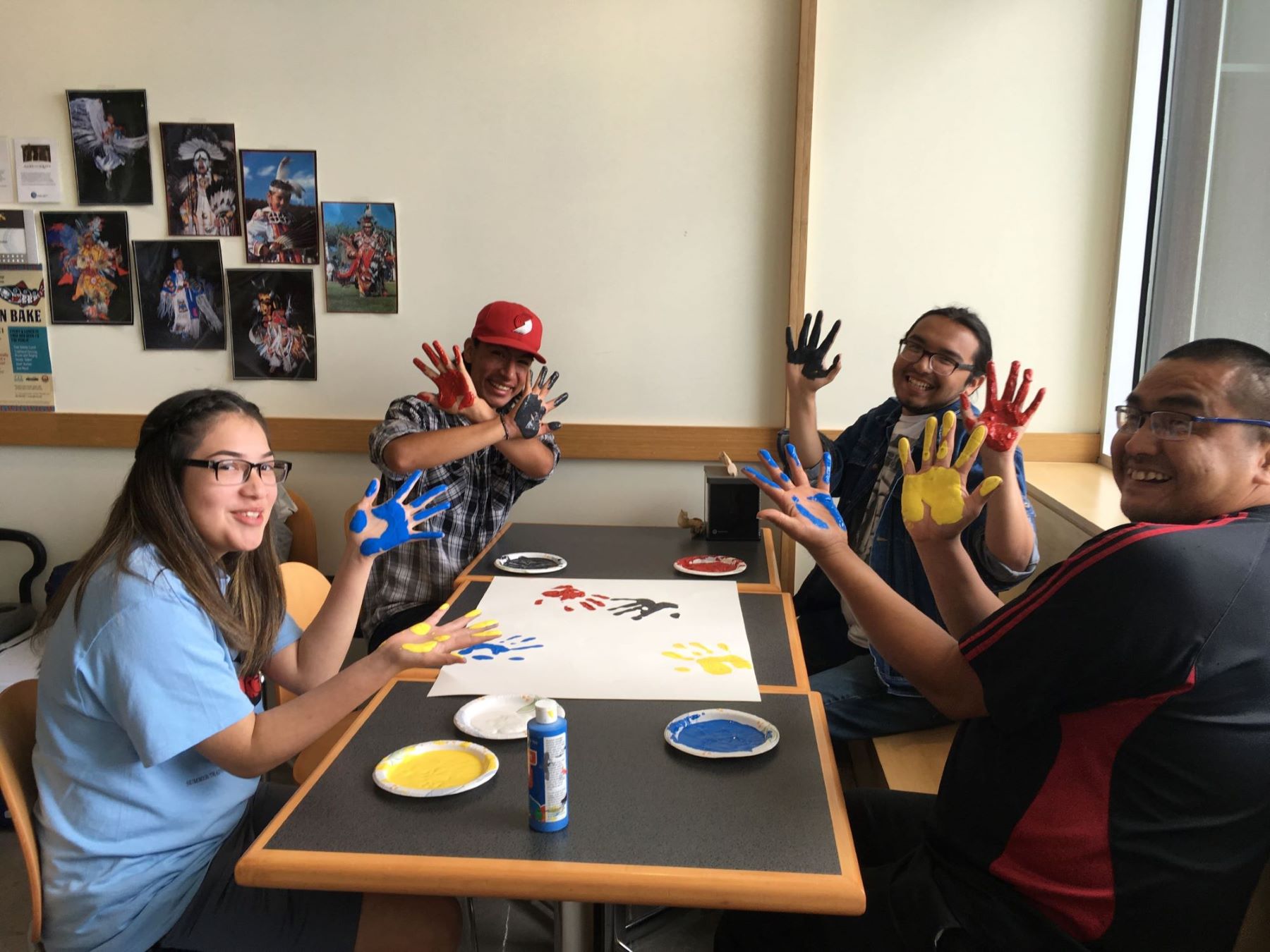 Native American high school students seated at table smiling and showing painted palms of hands.