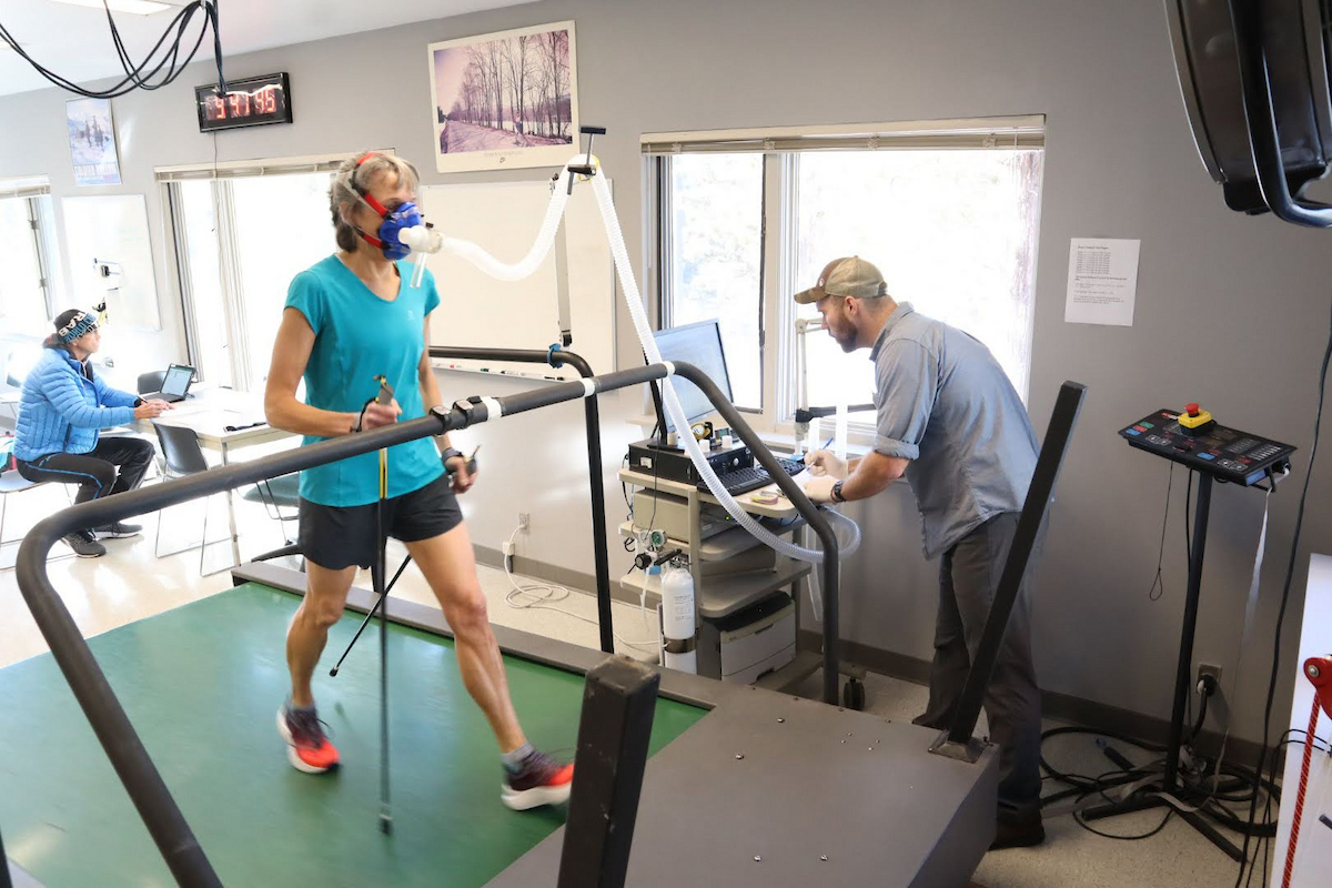 Woman walking on treadmill with mask to monitor oxygen as lab tech stands at computer 