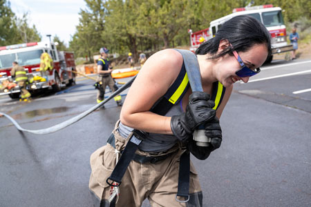 Female Fire Science student carrying hose and smiling