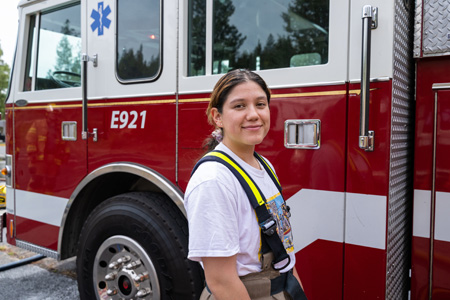 Female fire science student smiling in firefighter bibs in front of a fire truck