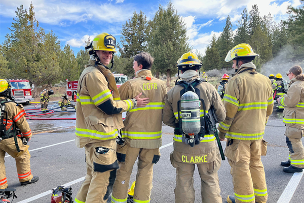 Central Oregon COmmunity College Fire Science students dressed in fire uniforms in parking lot with fire trucks in the background