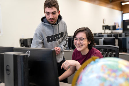 Geographic Information Systems students working together on a computer, female student is smiling and male student appears to be working the mouse.
