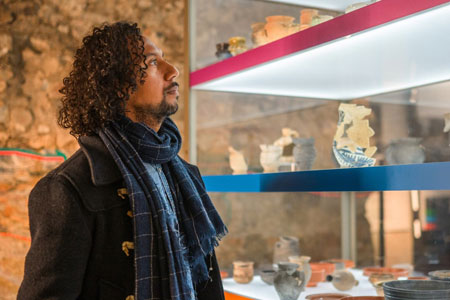 Male history professional with black curly hair admiring artifacts in a museum